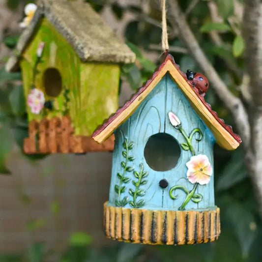 Nichoir décoratif en résine colorée Nest-oo Élégance Nature, suspendu à un arbre, attirant des mésanges dans un jardin lumineux.