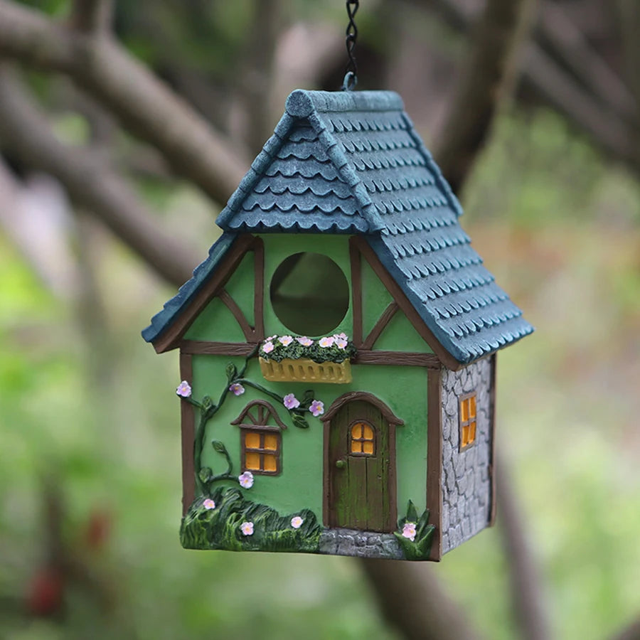 Nichoir suspendu en résine Nest-oo Jardin Bohème, suspendu à une chaîne noire dans un jardin verdoyant.