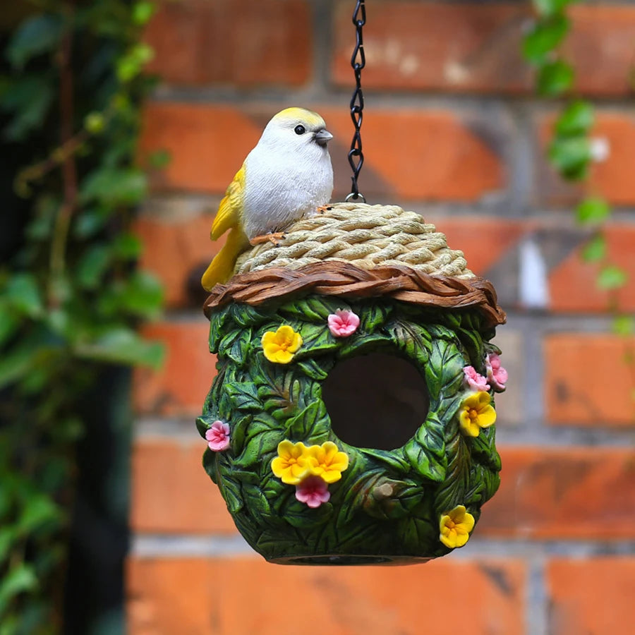 Nichoir suspendu en résine Nest-oo Jardin Bohème, suspendu à une chaîne noire dans un jardin verdoyant.