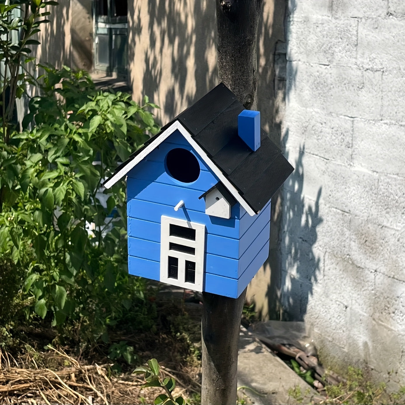 Nichoir coloré Spring Melody en bois léger suspendu dans un jardin fleuri, accueillant des mésanges et des bleuets.